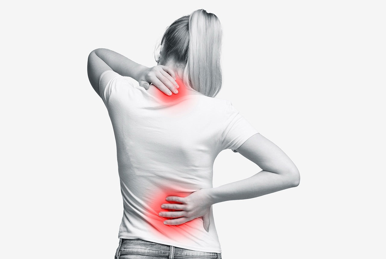 Frau fässt sich an den Rücken und deutet Schmerzen. 